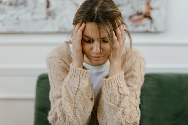 a woman sitting, holding her head, looking sad