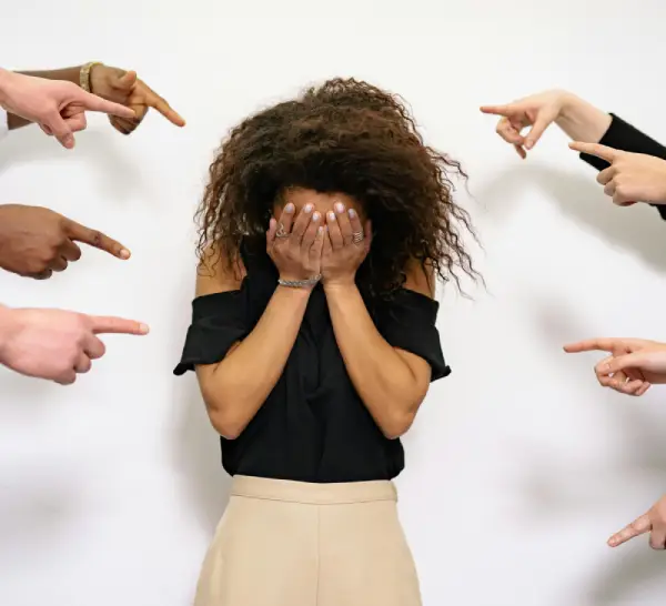 a black woman standing, hiding her face , getting point by different people