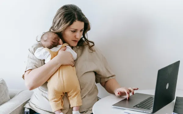 a woman carrying an infant while working on her laptop