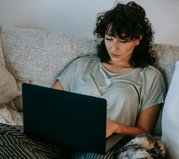 a woman sitting on her couch using a black laptop searching for jobs online