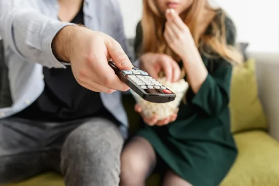 a couple trying to watch a movie, holding a remote control - one of cheap date ideas